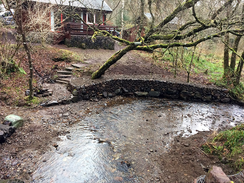 A nice example of a drystone retaining wall running along a small burn and stonework on a chalet 